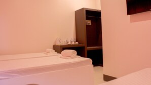 A hotel room with two beds, a wardrobe, a small table with toiletries, and a TV mounted on the wall. - Butuan Grand Palace Hotel Annex (Butuan)