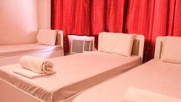 A hotel room with two single beds, each with a white mattress and pillow, and a red curtain in the background.