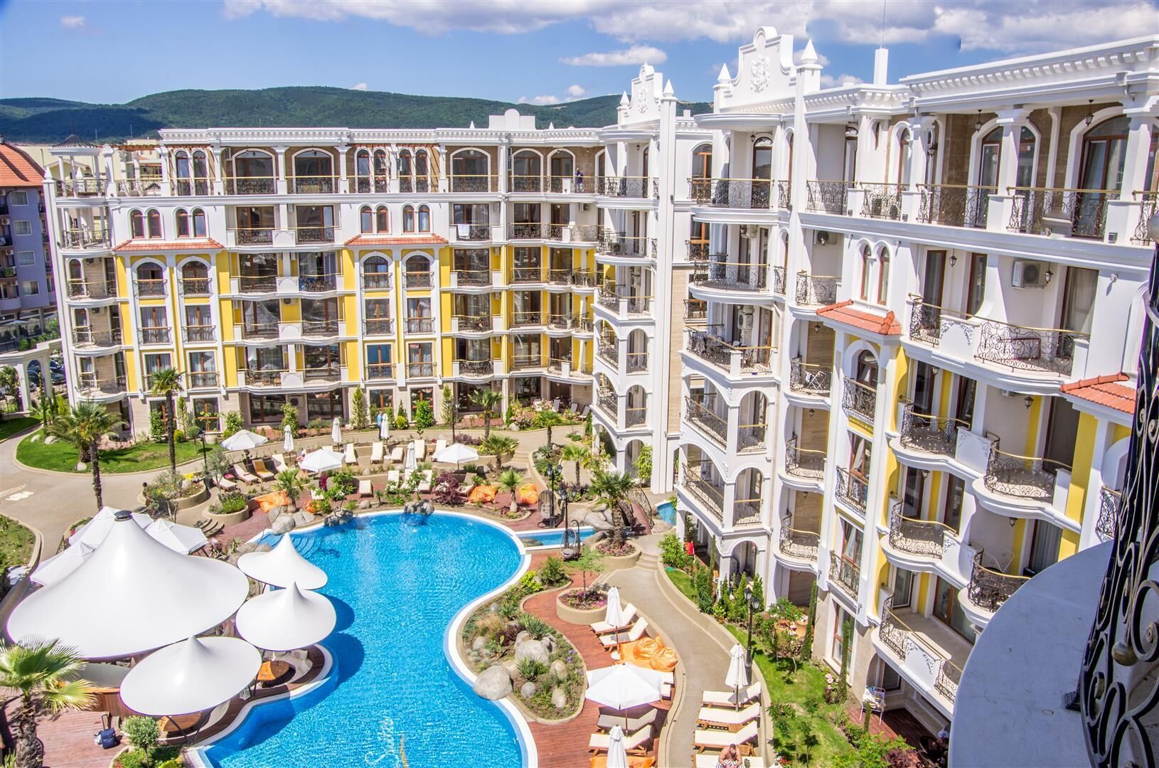 A hotel with multiple balconies, a central swimming pool, and outdoor seating areas.