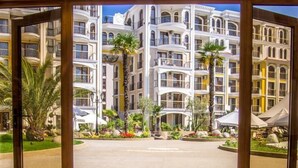 L’entrée d’un hôtel avec un sol réfléchissant, une grande porte en arc de cercle et une vue sur des immeubles à plusieurs étages dotés de balcons et de palmiers.