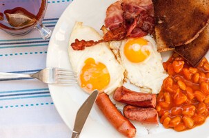 En tallrik med ägg, bacon, korv, bönor, rostat bröd och en kopp te.
