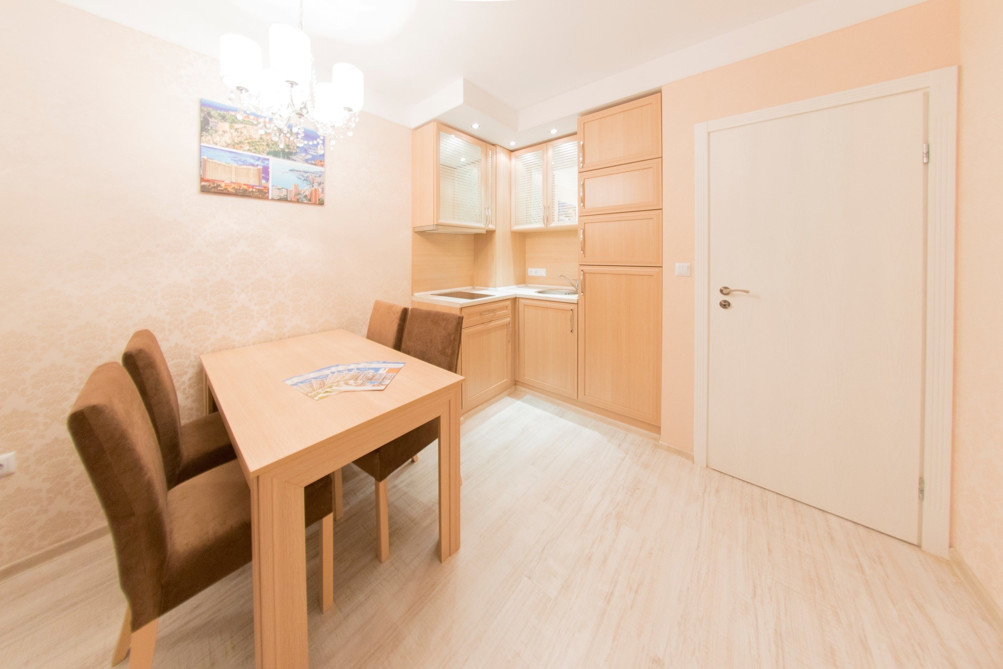 A compact kitchen with wooden cabinets, a dining table with chairs, and a door.