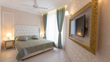 A bedroom with a tufted headboard, a bed with patterned bedding, a television mounted on the wall, and a ceiling fan.