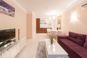 A modern living room with a flat-screen TV, a white coffee table, a purple sofa, and a dining area with a table and chairs.