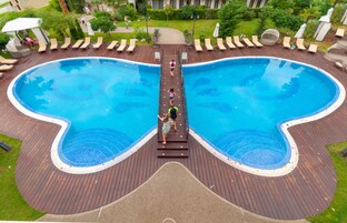 A large, uniquely shaped swimming pool with a wooden deck and lounge chairs around it.