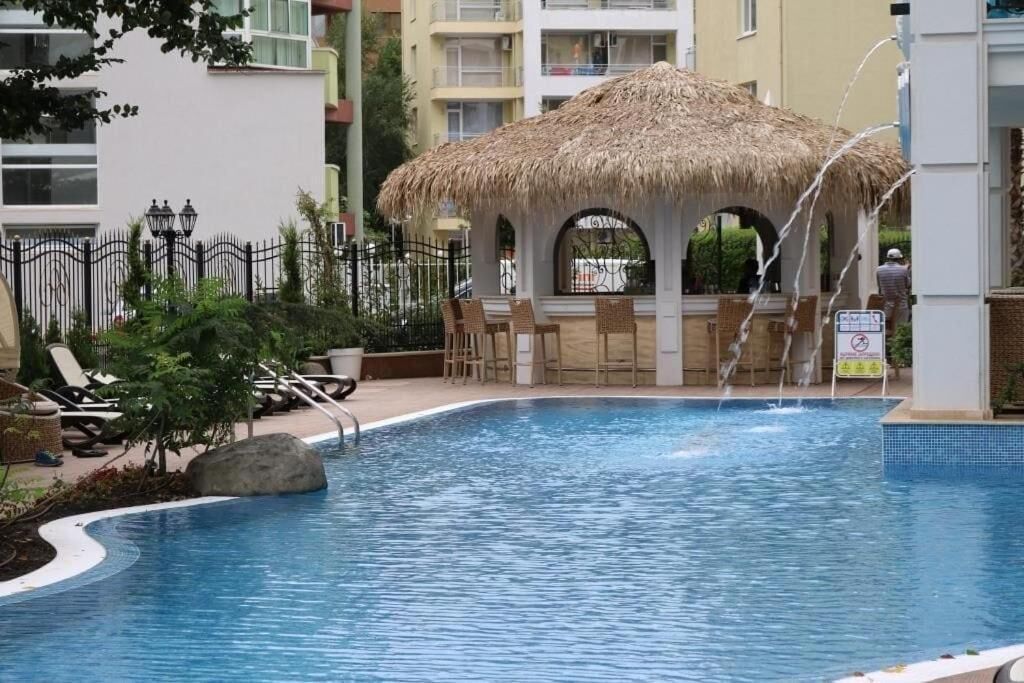 A swimming pool with lounge chairs and a thatched-roof gazebo.