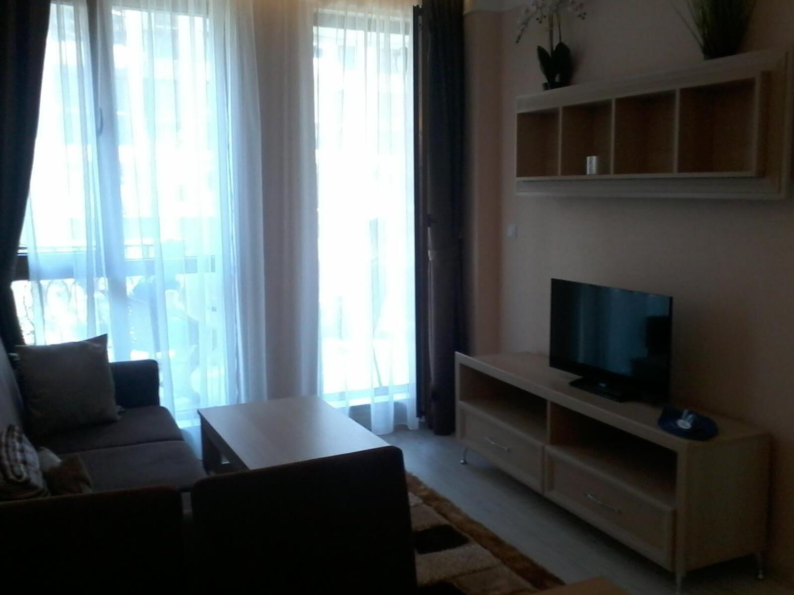 A living room with a sofa, a TV on a stand, and a large window with curtains.