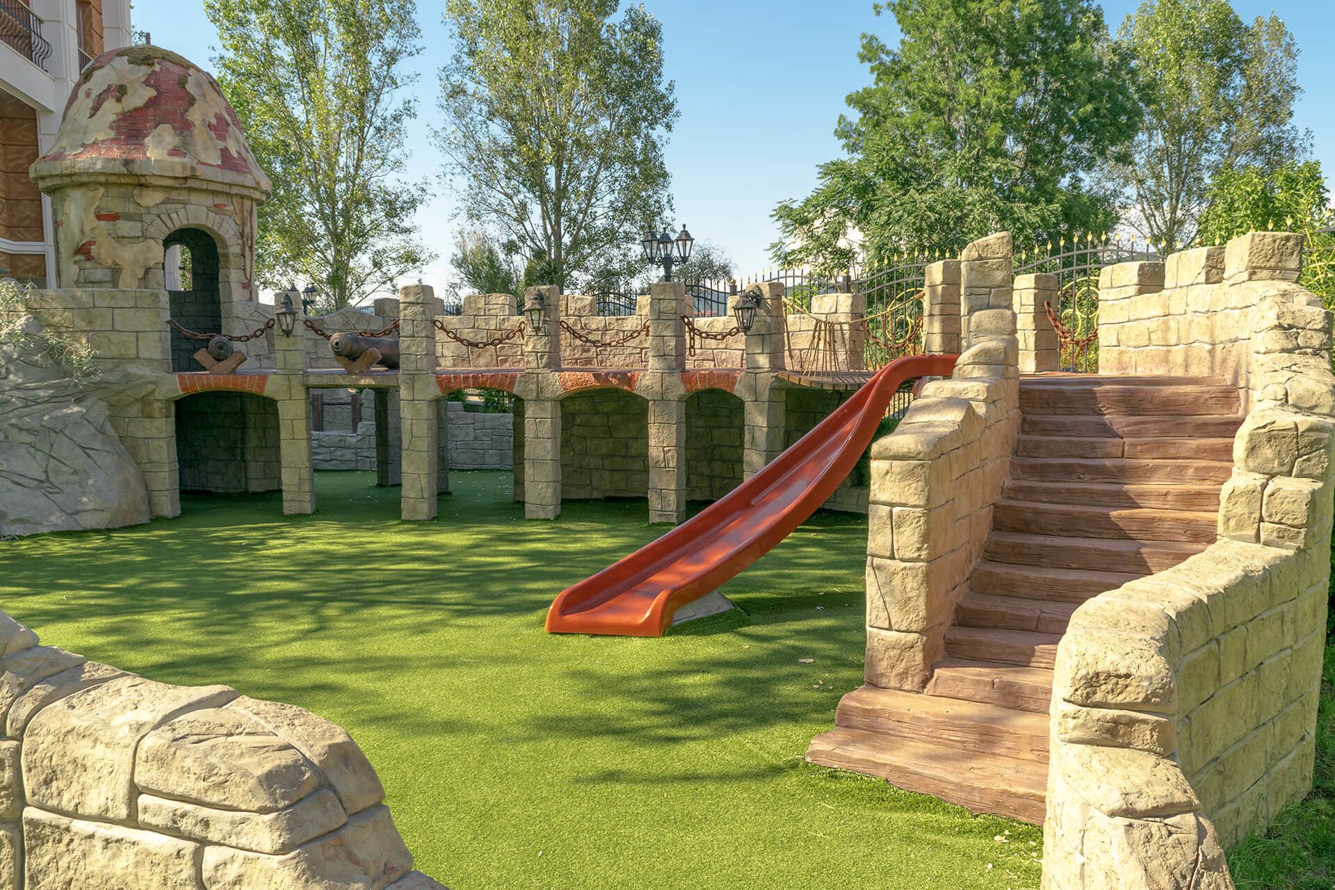 A playground with a red slide, stone structures, and a grassy area.