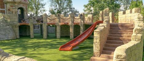 A playground with a red slide, stone structures, and a grassy area.
