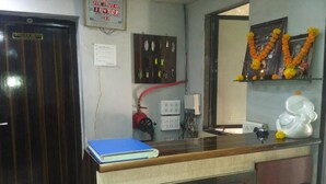 Una habitación con mostrador de madera, un cuaderno azul, un reloj, un panel eléctrico en la pared y una estantería con adornos.