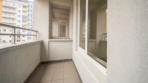 A narrow balcony with a tiled floor, a window, and a view of a building in the background.