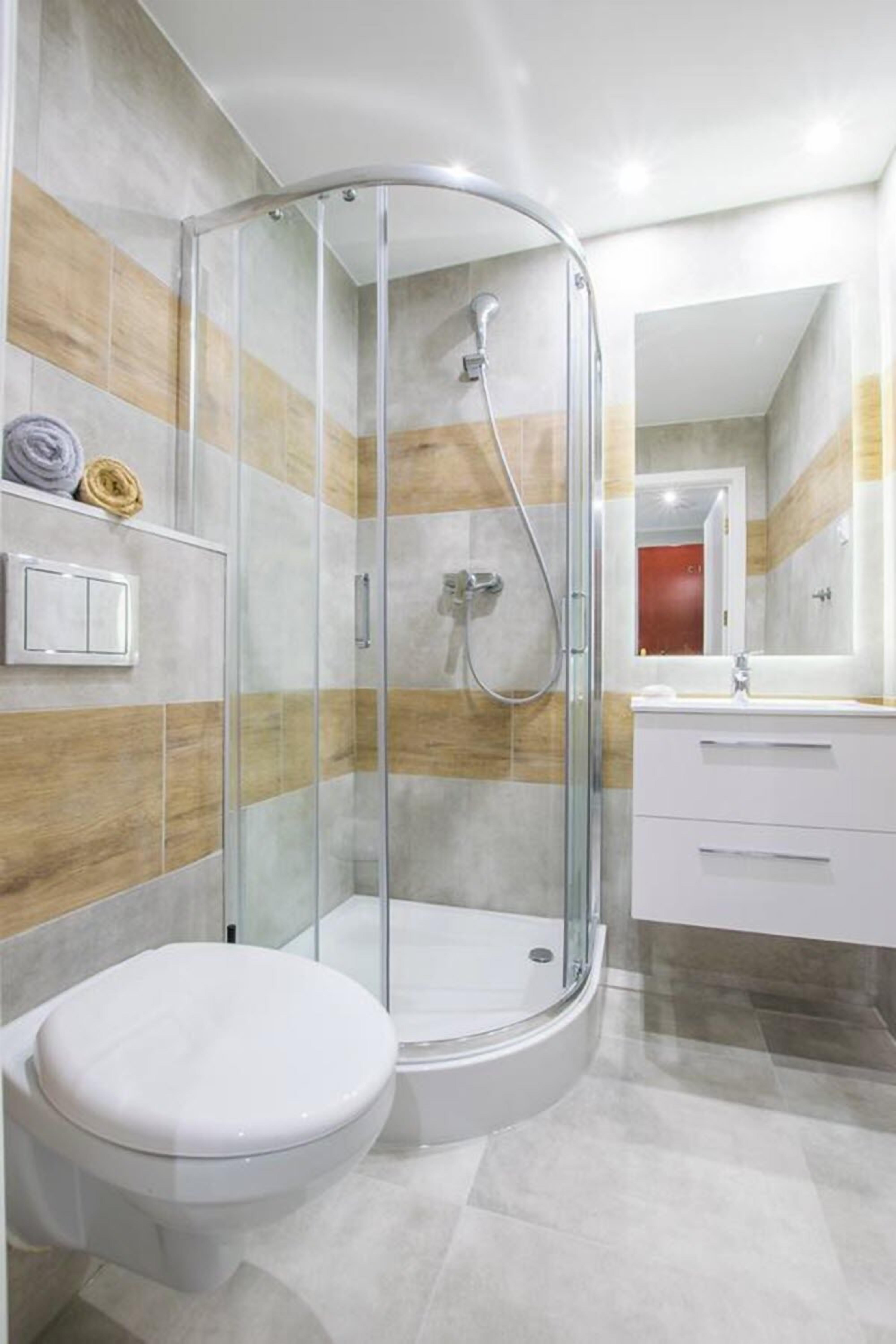 Een moderne badkamer met een douchecabine van glas, een wit toilet en een wastafel met spiegel.