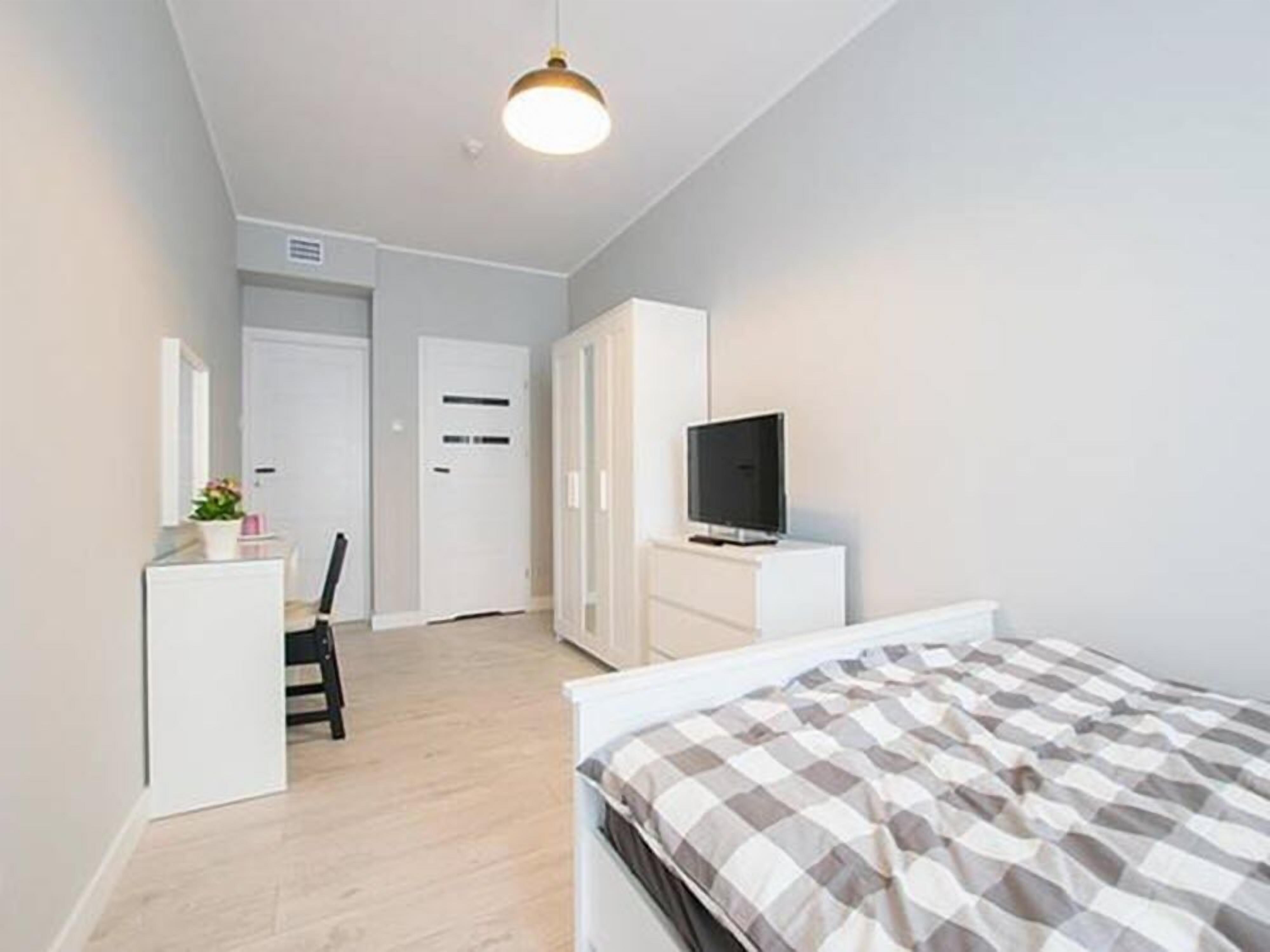 Une chambre à coucher avec un lit, un téléviseur posé sur un meuble, une armoire et un bureau avec une chaise.