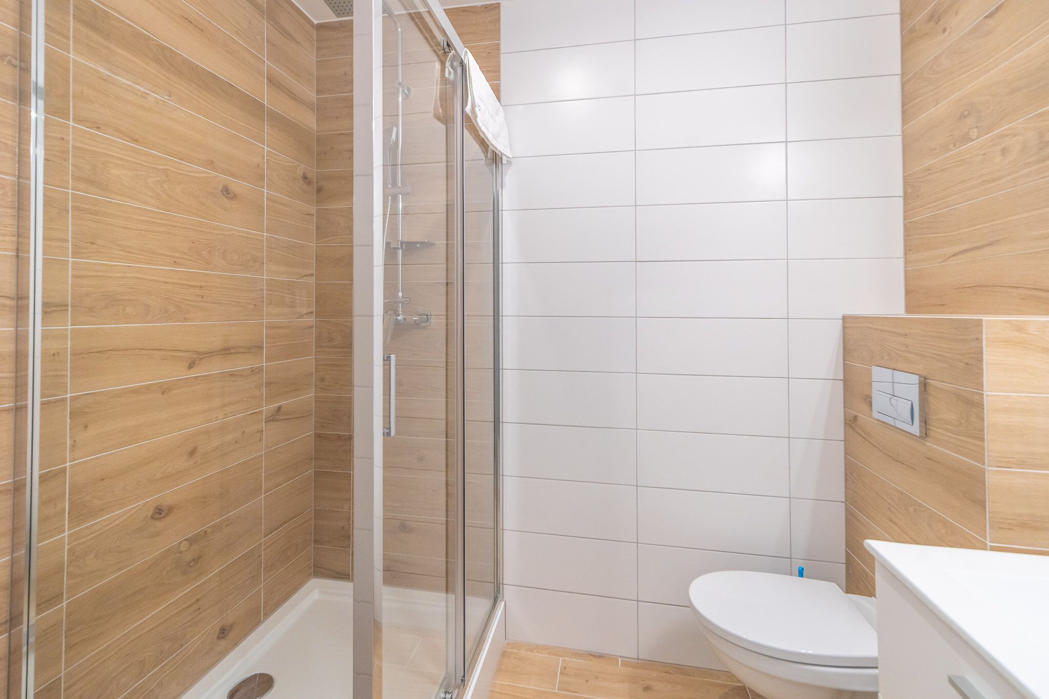 Une salle de bain moderne avec une douche à parois de verre, des carreaux blancs et un lambris en bois.