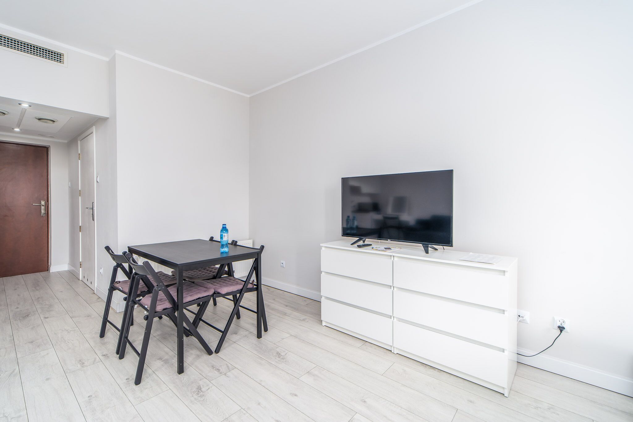 Una sala moderna con una mesa de comedor, sillas, un televisor de pantalla plana y un mueble de almacenamiento blanco.