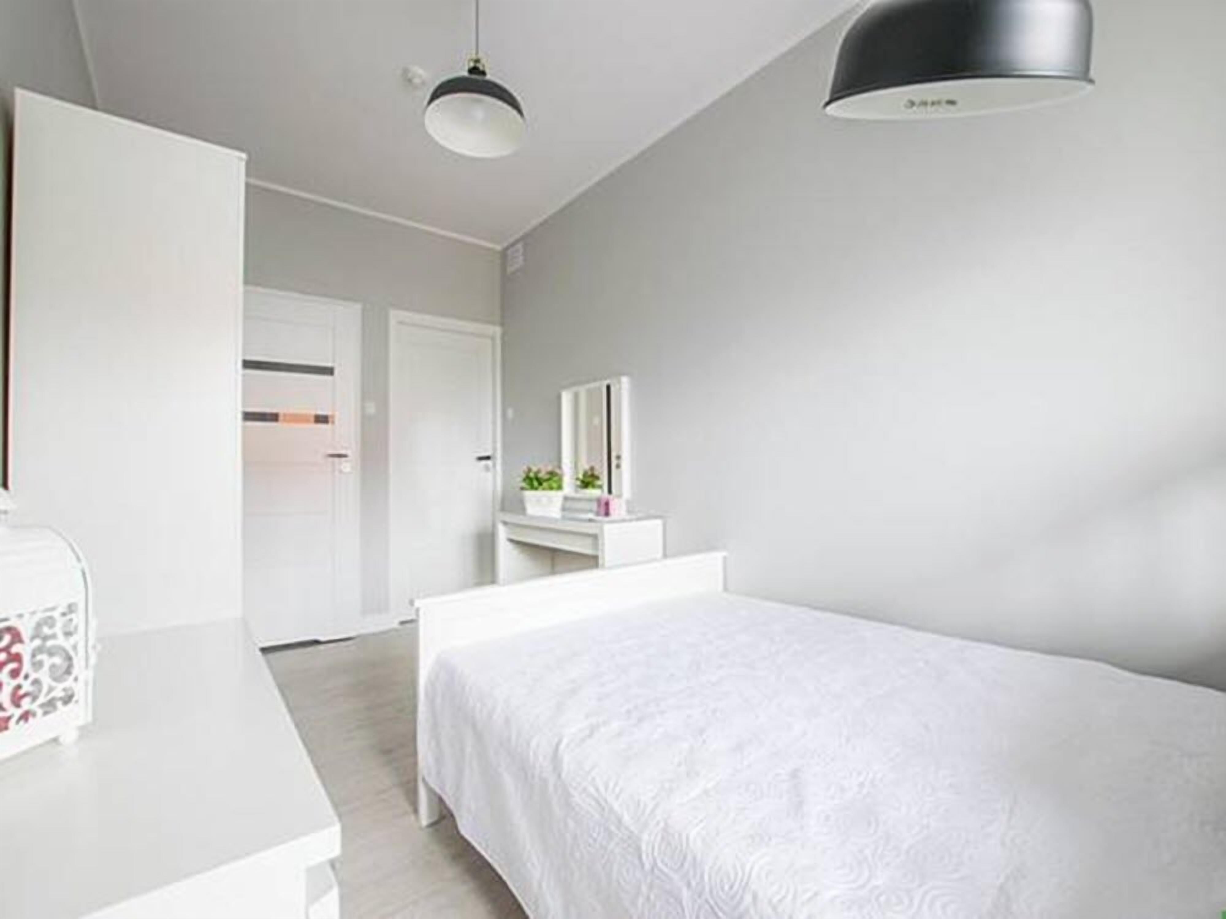 A modern bedroom with a large bed, a bedside table, a dresser, and a mirror.