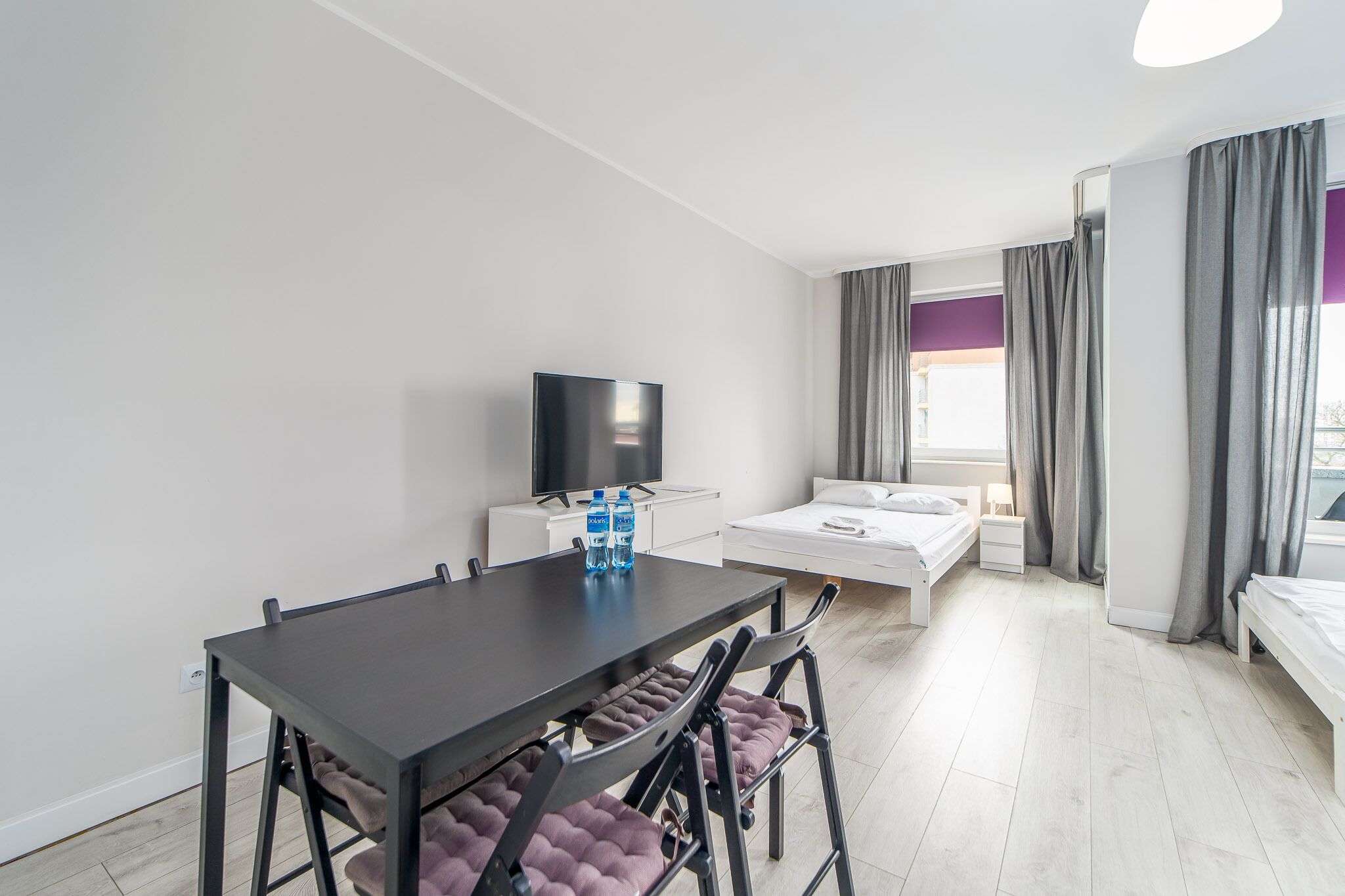 Une chambre d’hôtel moderne équipée d’une table à manger, de deux lits, d’un téléviseur et d’une fenêtre avec des rideaux.