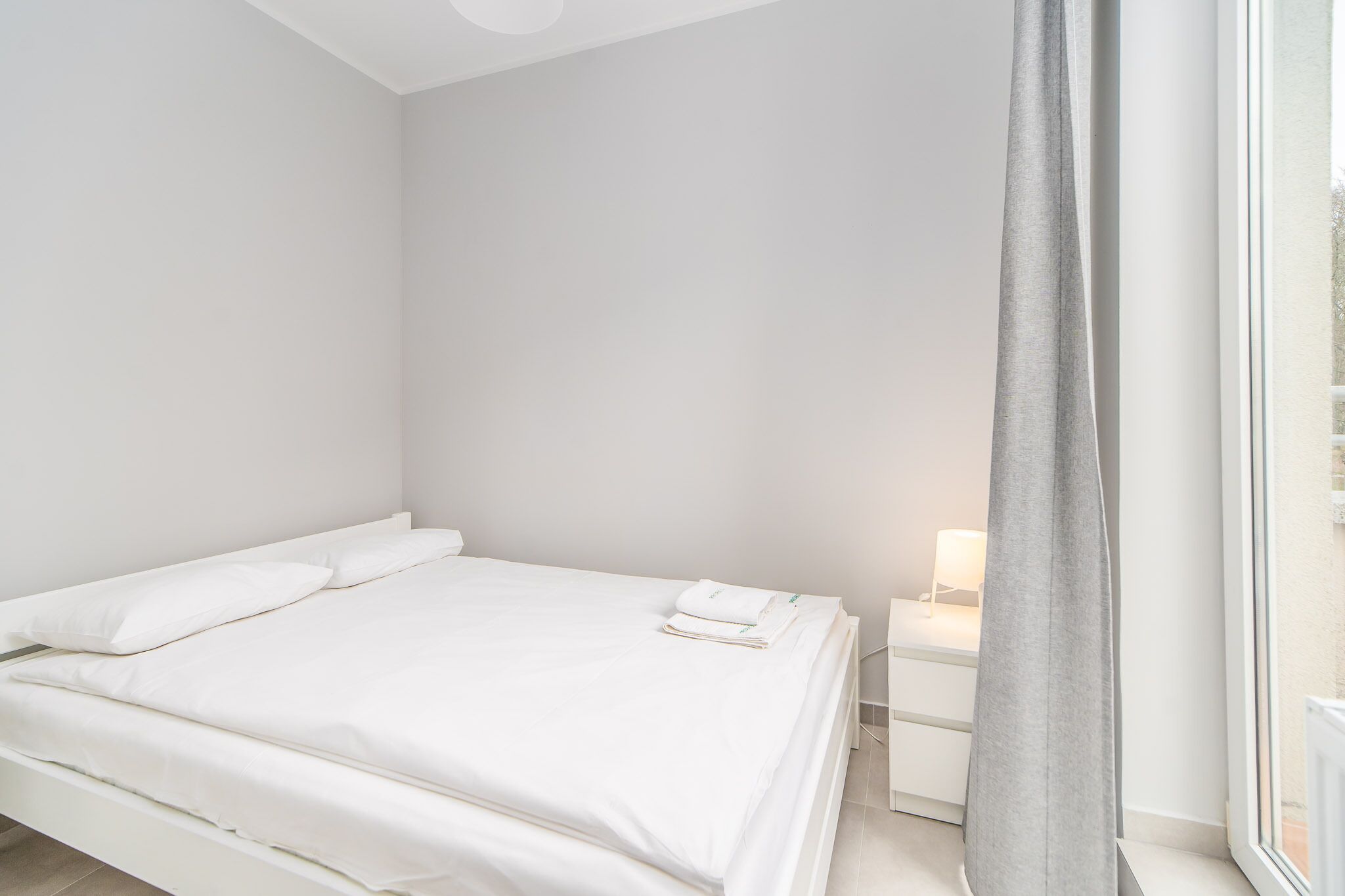 Camera da letto minimalista con un letto, comodino e una finestra con tenda.