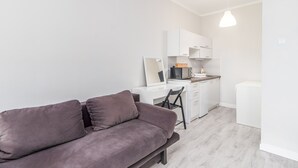 A modern living room with a grey sofa, a small kitchen area with white cabinets, and a dining table.
