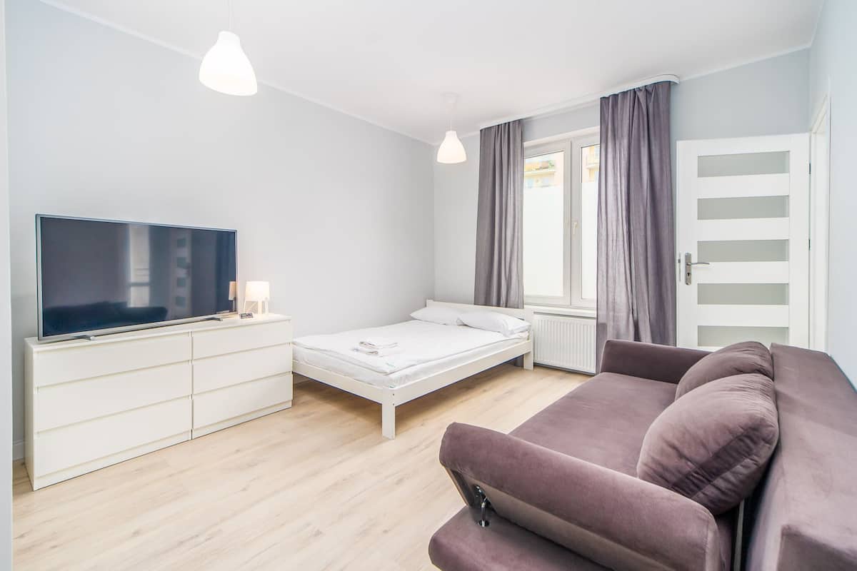 Ein modernes Schlafzimmer mit Bett, Fernseher, Sofa und einem Fenster mit Vorhängen.