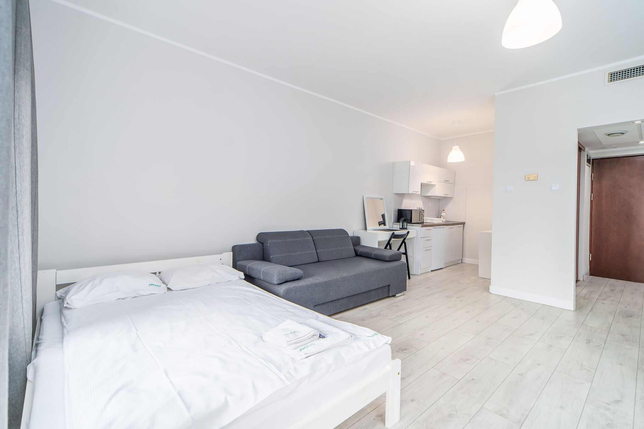 A modern, minimalistic bedroom with a bed, a grey sofa, a desk, and a wardrobe.