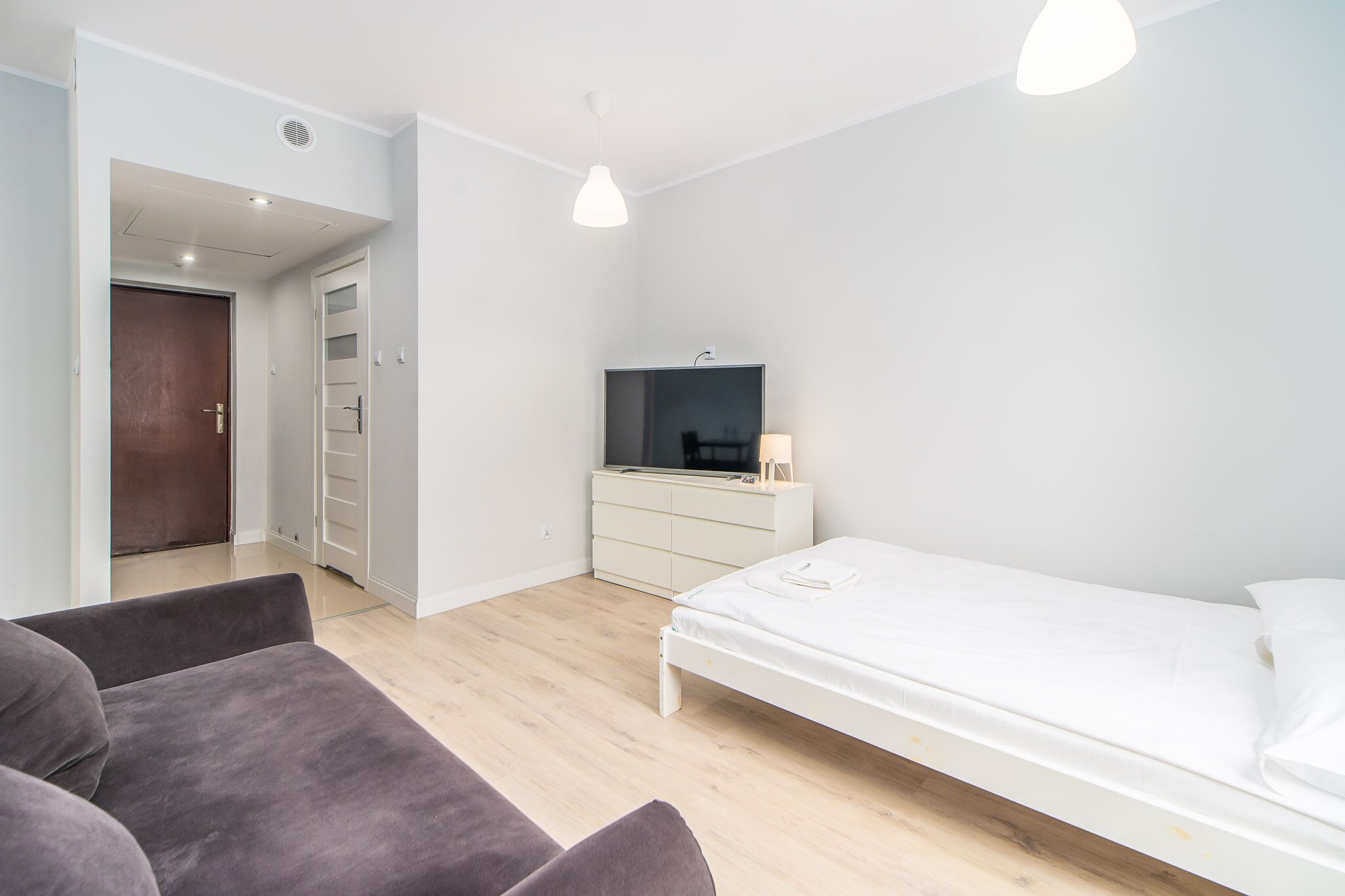 A modern bedroom with a bed, a TV, a dresser, and a sofa.