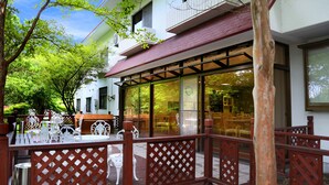 A building with a red awning, outdoor seating area with white chairs and tables, and a wooden fence. - Asia Hotel Fujisan (Yamanakako)