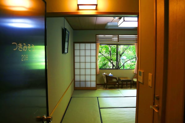 Una habitación japonesa tradicional con suelo de tatami, un divisor shoji y vistas a la vegetación exterior.