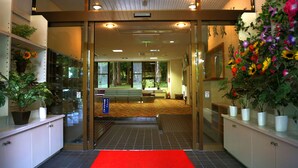 A hotel lobby with a red carpet, glass doors, potted plants, and a reception desk. - Asia Hotel Fujisan (Yamanakako)