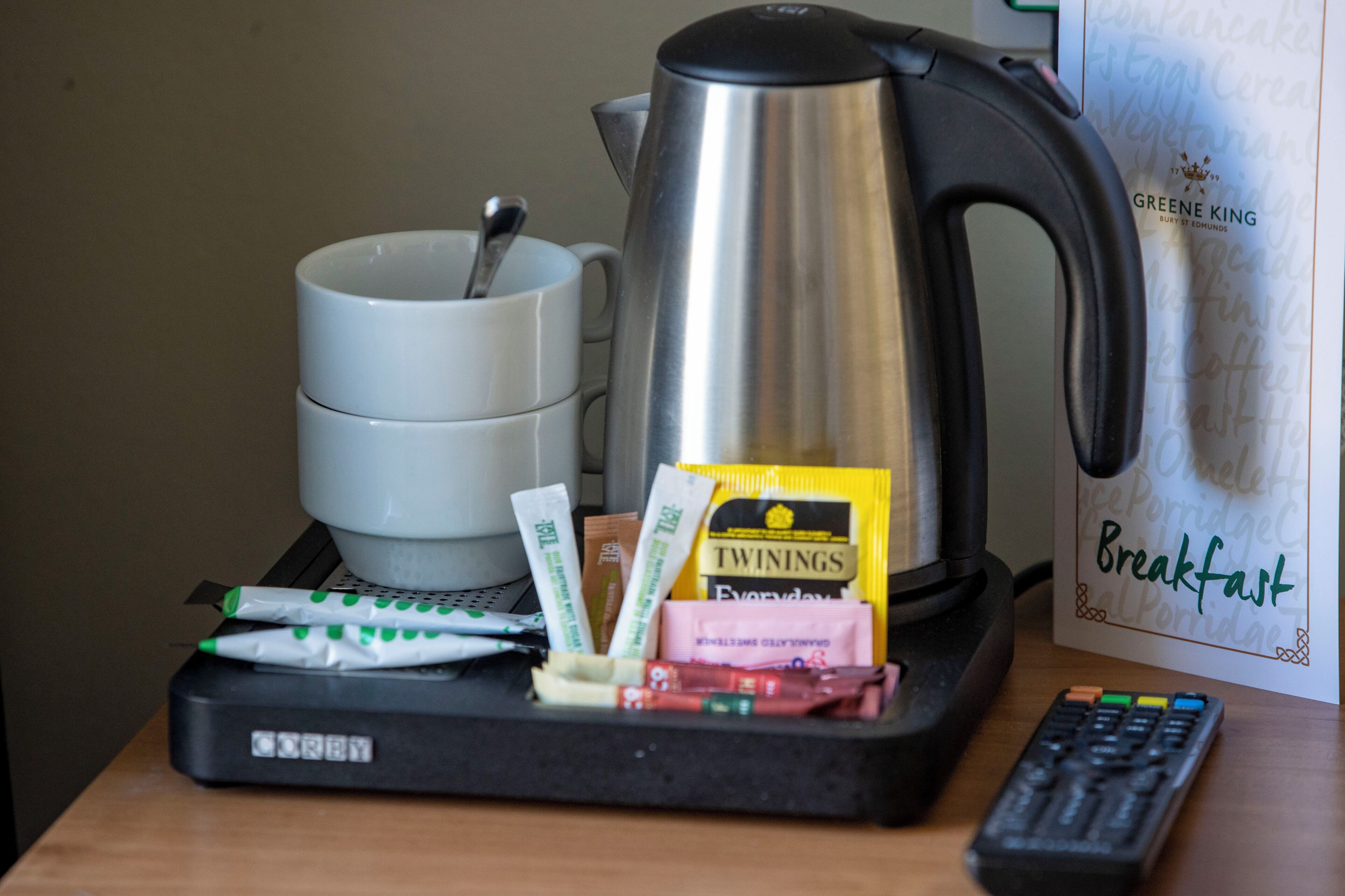 A breakfast tray with a coffee pot, cups, and food packets on a table.