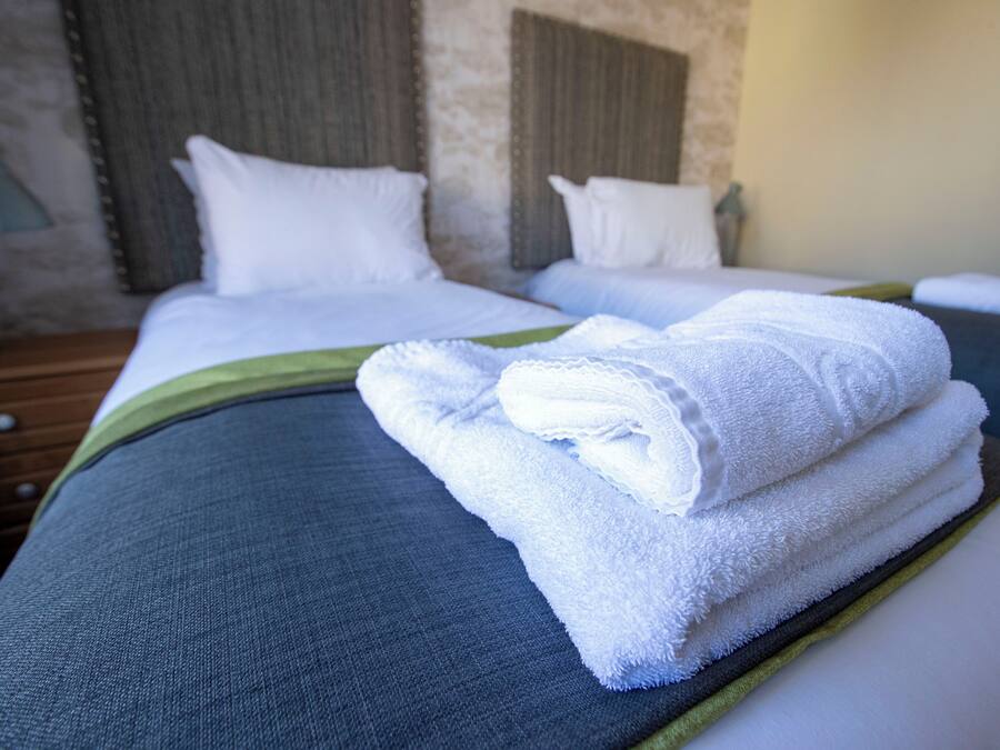 A hotel room with two beds, each with white linens and pillows, and a green accent on the bedspread.
