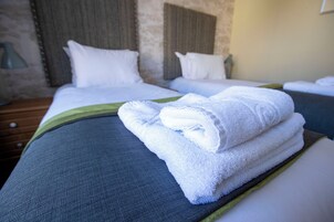 Quarto de hotel com duas camas, cada uma com roupa de cama e almofadas brancas, e um detalhe verde no edredom.