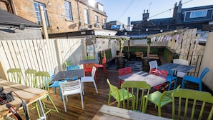 Un espace extérieur aménagé en terrasse, avec des tables et des chaises en bois, un petit coin salon et une vue sur les bâtiments environnants.