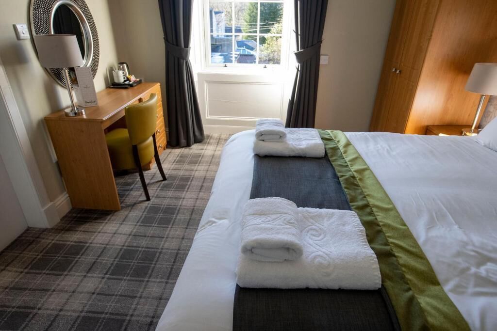 Una habitación de hotel con cama, escritorio, silla y ventana con cortinas.