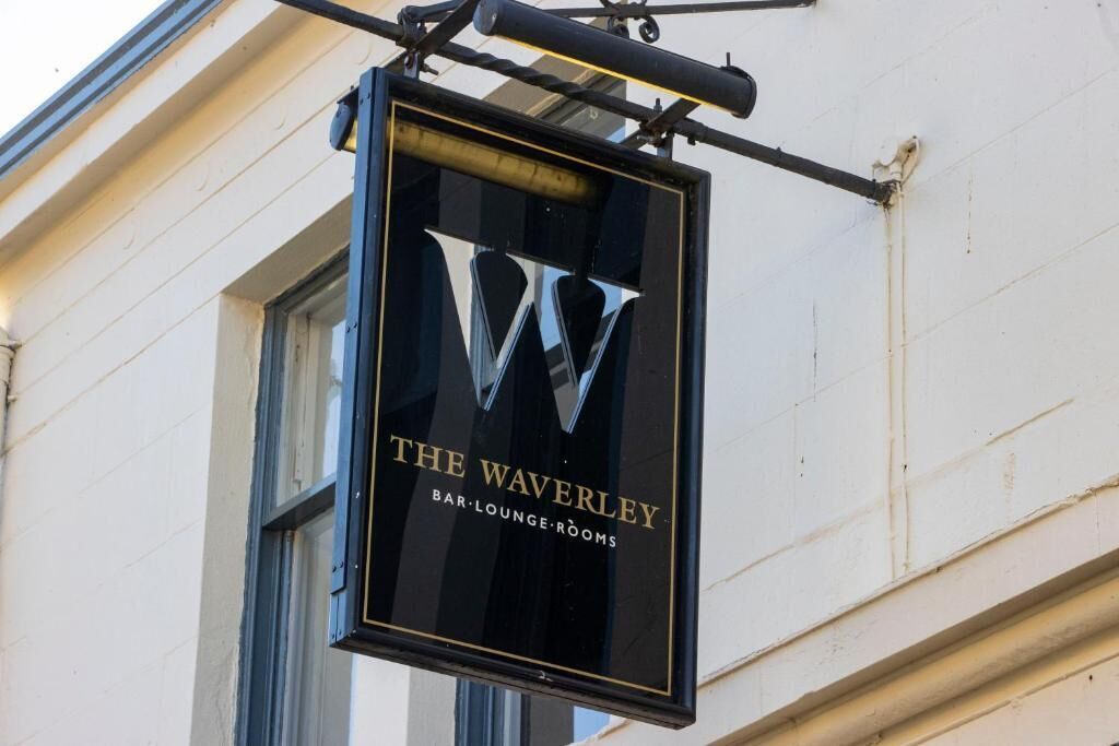 Un letrero colgante para 'The Waverley Bar Lounge Rooms' con un llamativo logo 'W'.