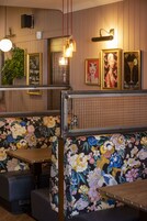 Interior de restaurante com cabines estampadas com flores, luminárias pendentes e quadros nas paredes.