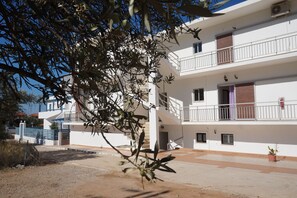 A multi-story white building with balconies, a gated entrance, and a clear sky. - Yialos Studios (Agistri)