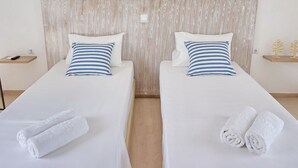 Two single beds with white bedding and blue-striped pillows, a wooden headboard, and white towels on each bed. - Yialos Studios (Agistri)