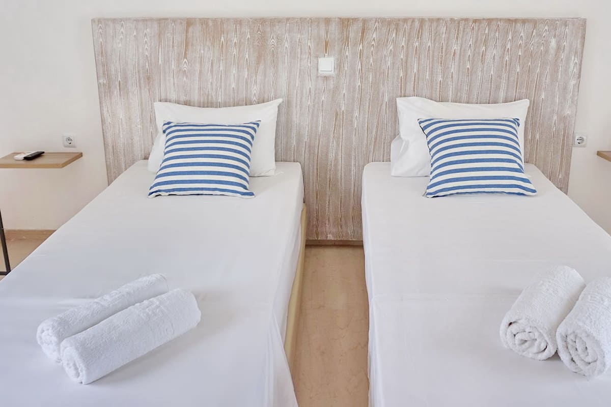 Two single beds with white bedding and blue-striped pillows, a wooden headboard, and white towels on each bed.