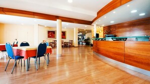 Un'area ristorazione moderna con pavimento in legno, una reception e diversi tavoli con sedie.