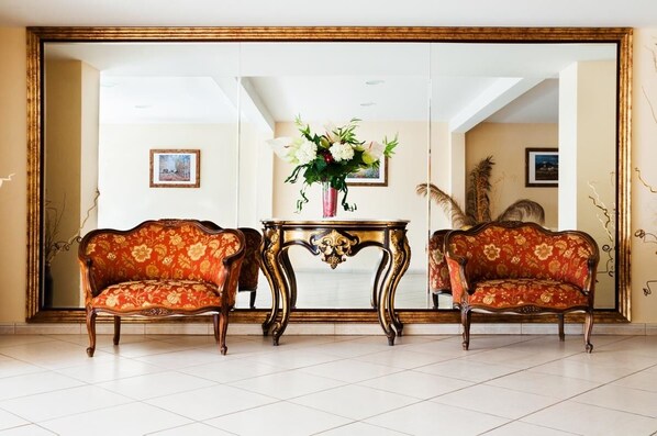 Una habitación con dos sofás decorados, una mesita con un florero y un espejo grande en la pared.