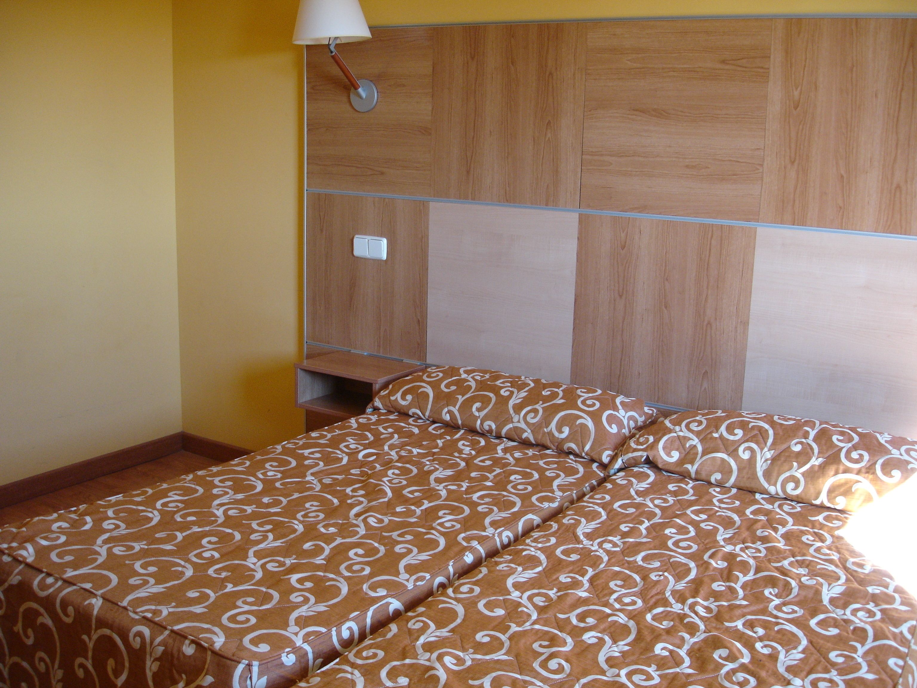 Habitació amb un llit, una tauleta de nit i una làmpada penjada a la paret.