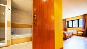 Camera d'albergo con una porta in legno, una vasca da bagno, un letto con copriletto decorato, una finestra con tende e una sedia.