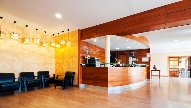 Zona reception di un hotel con scrivania in legno, sedute in pelle nera e lampade a sospensione.