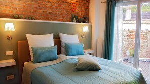 Un dormitorio con pared de ladrillo, dos mesitas de noche con lámparas, una cama con ropa de cama azul y vistas a un patio a través de una puerta corrediza.