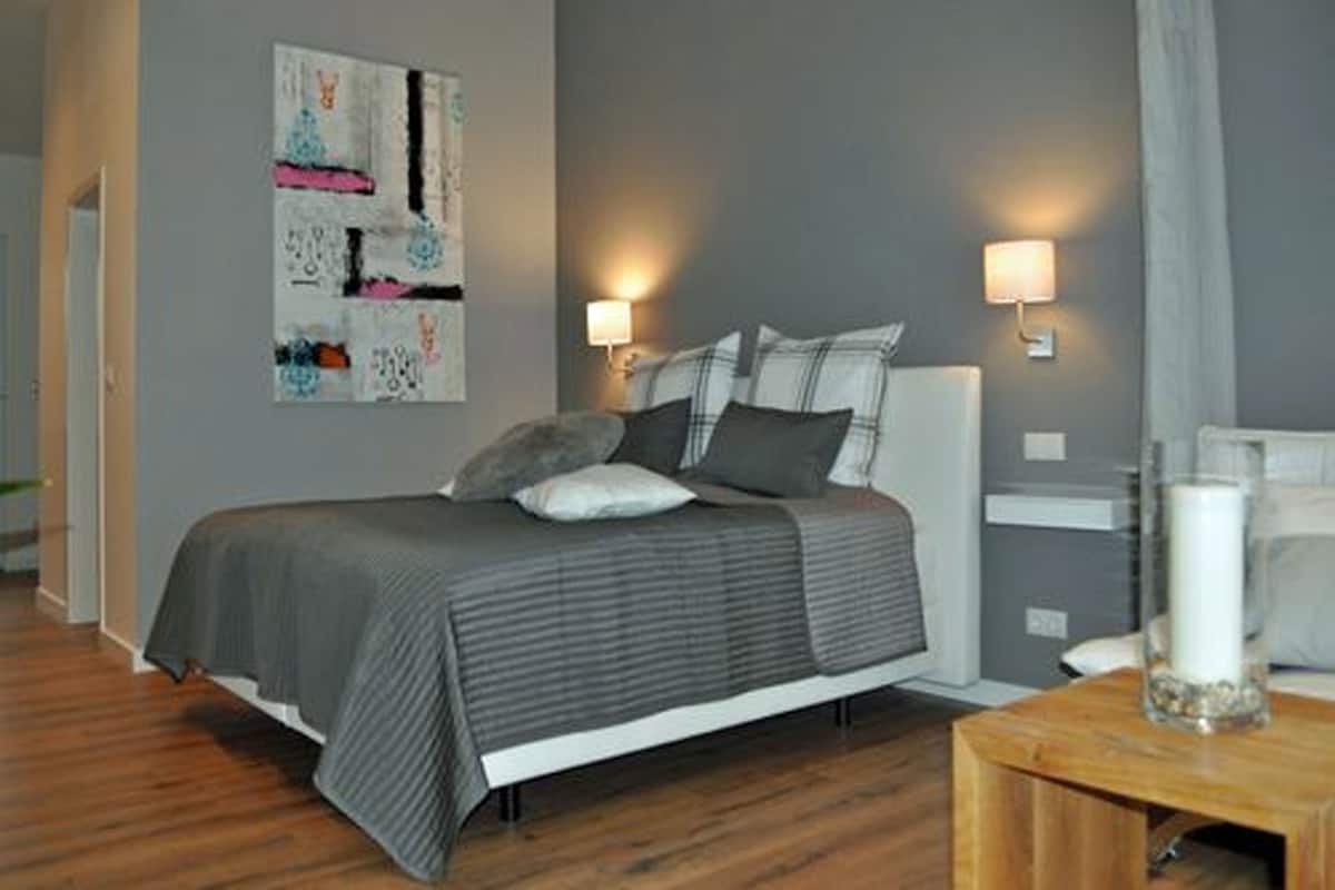 A modern bedroom with a bed, bedside lamps, and a decorative wall piece.