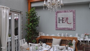 Un comedor acogedor con un banco de madera, sillas blancas y una mesa dispuesta con vajilla blanca. Un candelabro cuelga del techo y un cuadro con las letras 