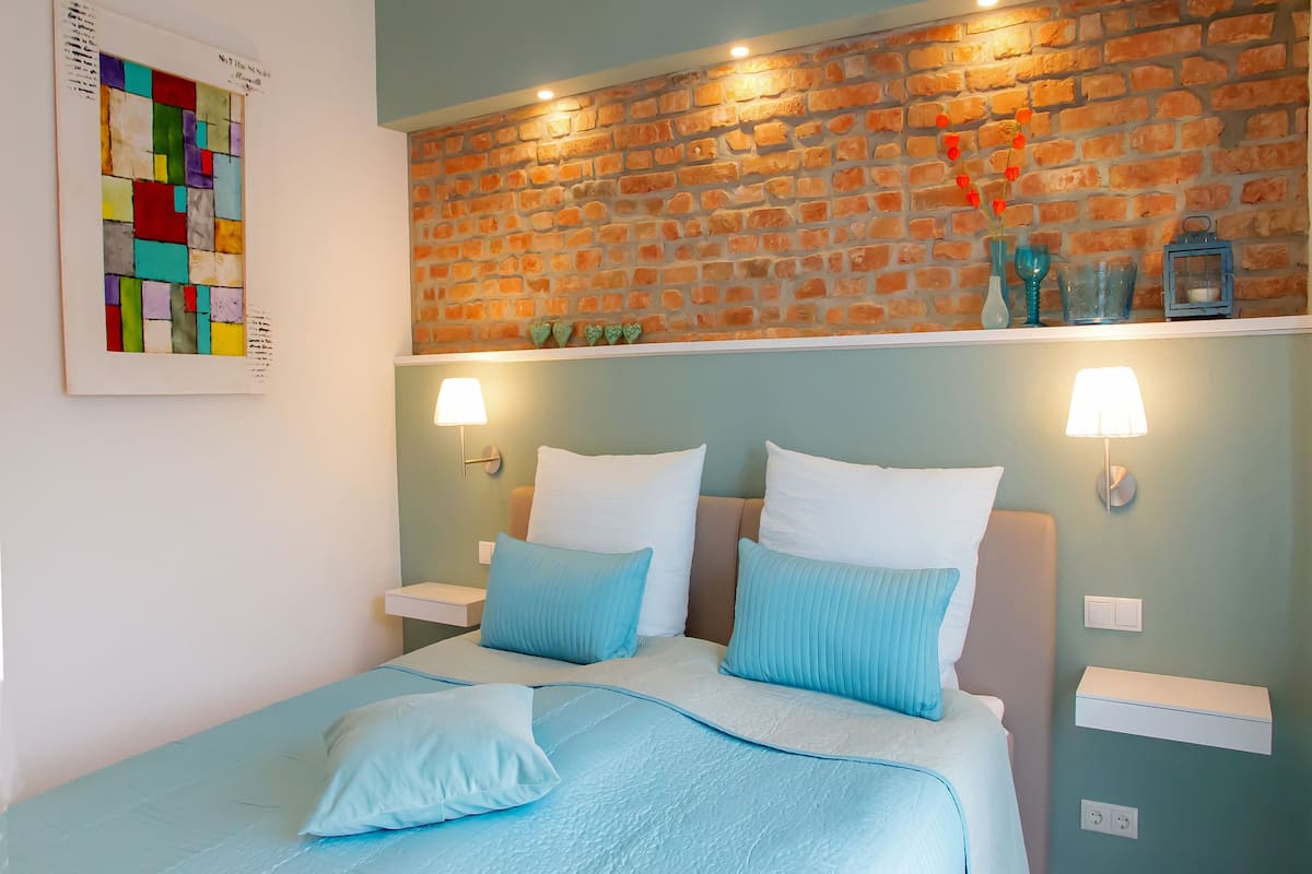 A bedroom with a brick-patterned headboard, a bed with blue bedding, two bedside lamps, and a wall-mounted artwork.