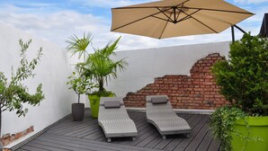 Una terraza en la azotea con dos sillones de relax, un paraguas grande, plantas en macetas y un muro de ladrillo.