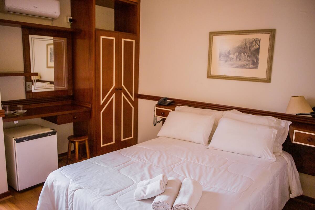 A hotel room with a bed, a desk, a refrigerator, and a mirror.